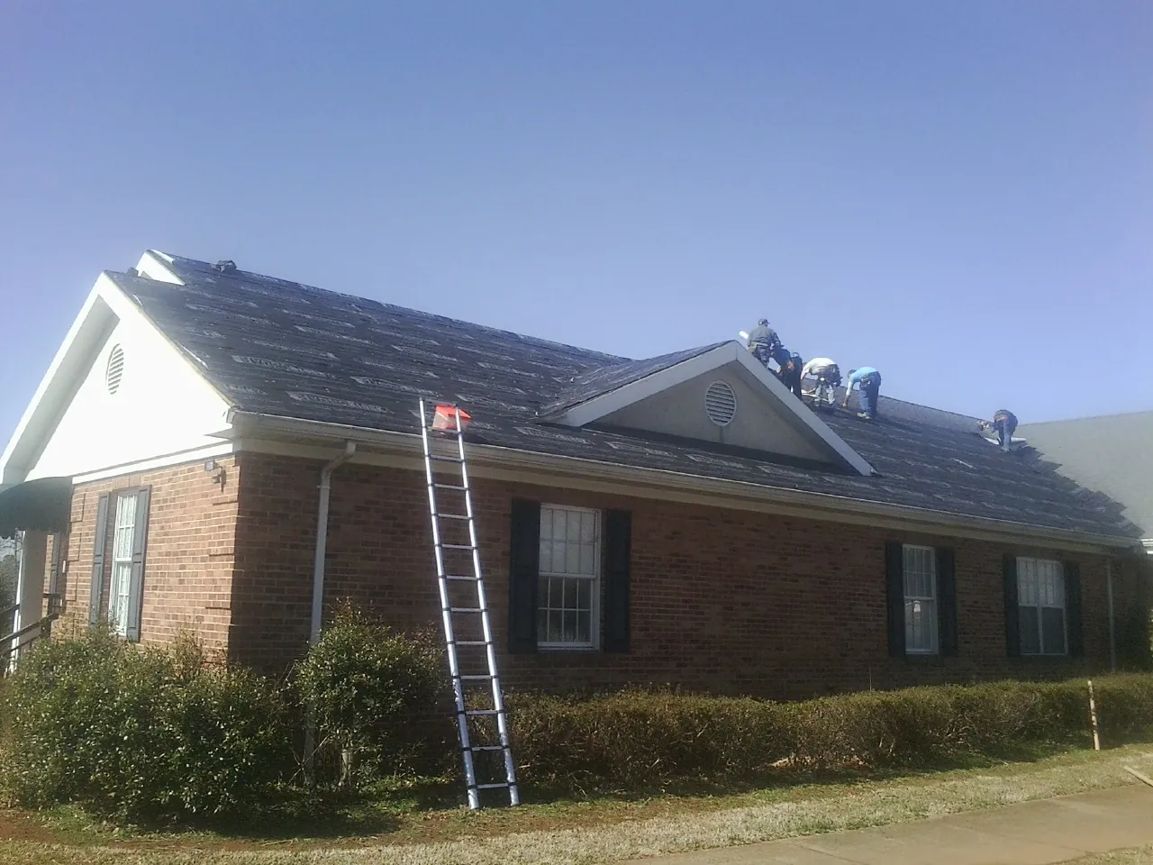 Crew tearing shingles off a brick ranch roof with a ladder set — Emergency Roof Repair work by our crew in Port Wentworth