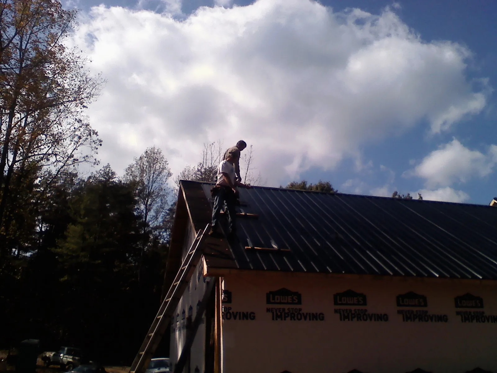 Roofer fastening dark metal panels high against a cloudy sky, from a Roof Inspection job in Port Wentworth