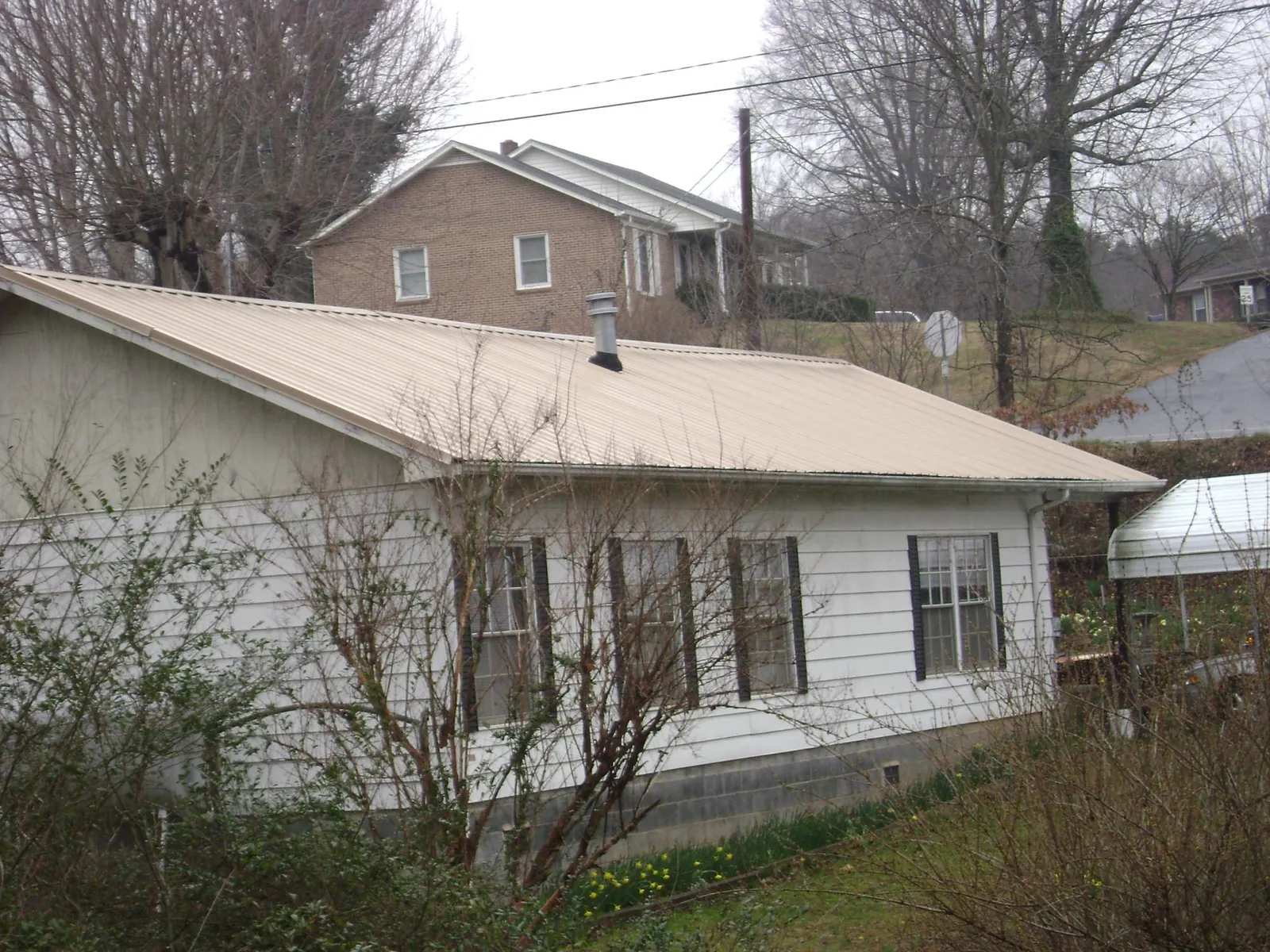 Tan metal roof on a white sided house set into a hillside — Commercial Roofing by Roofing Brothers in Port Wentworth