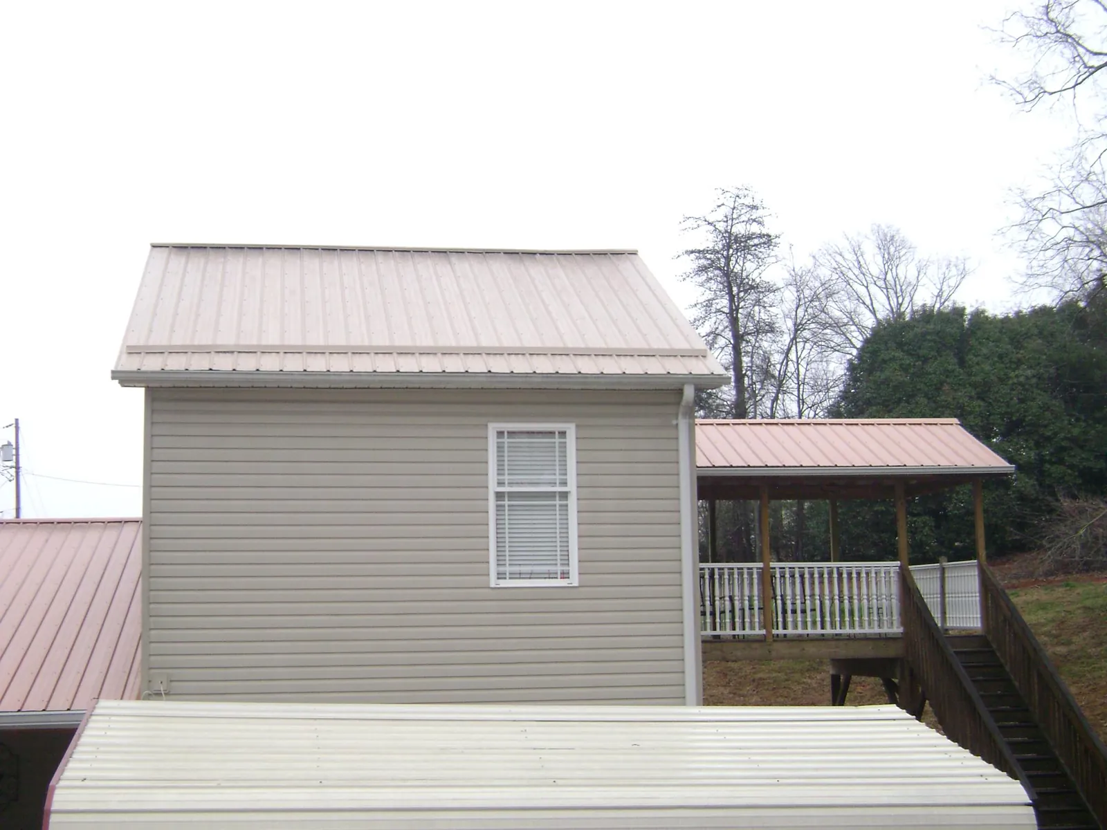 Tan metal roofs on a two story addition and attached porch, from a Roof Replacement job in Port Wentworth